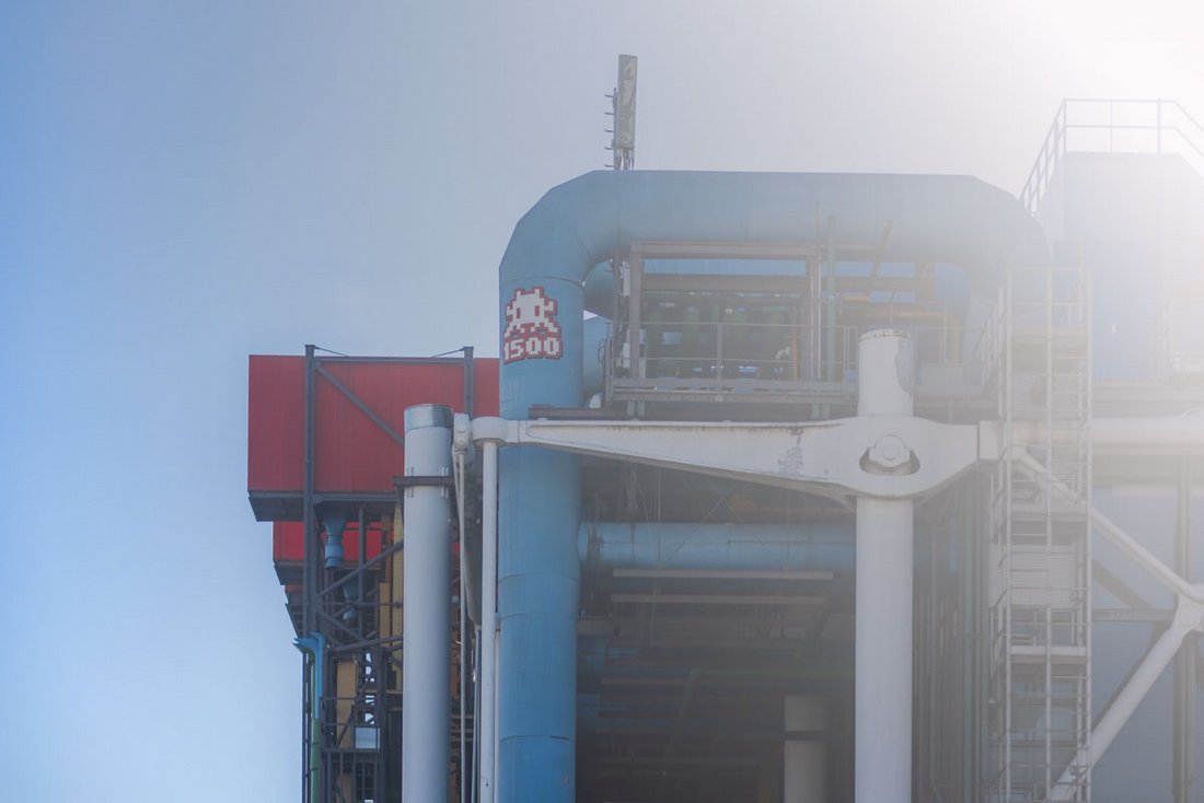 Sur la façade haute du Centre Pompidou, un petit personnage pixelisé rouge et blanc, typique de l’artiste urbain Space Invader, est incrusté sur un tuyau bleu clair. Ce motif numéroté “1500” s’inscrit dans la série mondiale d’invasions artistiques de l’artiste, mêlant culture pop et patrimoine architectural. Le contraste entre la rigueur industrielle du bâtiment – ses tuyaux apparents, ses passerelles métalliques et ses blocs colorés – et l’humour rétro du jeu vidéo crée une scène urbaine à la fois ludique et symbolique, emblématique du street art parisien.