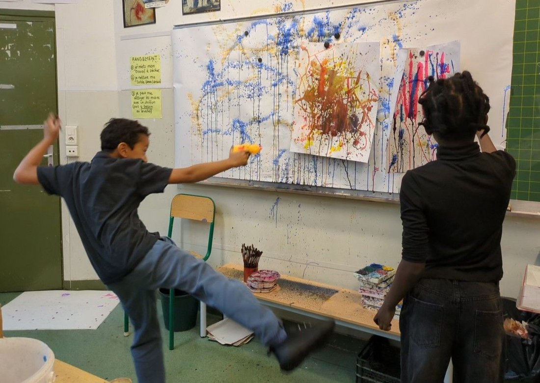 Atelier de pratique artistique à l'école : groupe d'enfants en train de peindre un tableau abstrait à coups de jets de peinture