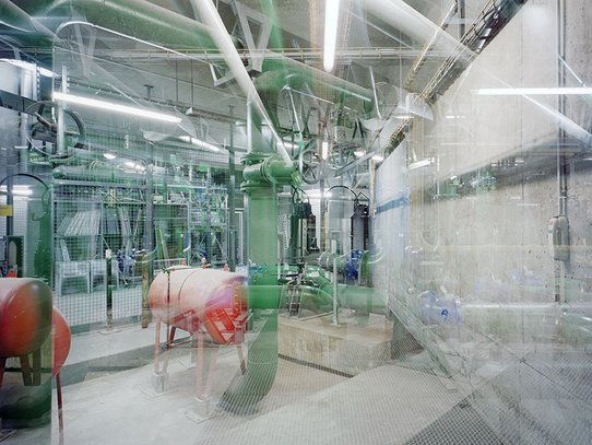 Au niveau -3 du Centre Pompidou, une salle technique se dévoile derrière un grillage métallique. Des tuyaux verts serpentent entre des vannes et des réservoirs rouges, dans une atmosphère industrielle feutrée. Le béton brut et les lumières blafardes accentuent la dimension souterraine et fonctionnelle de cette infrastructure cachée.