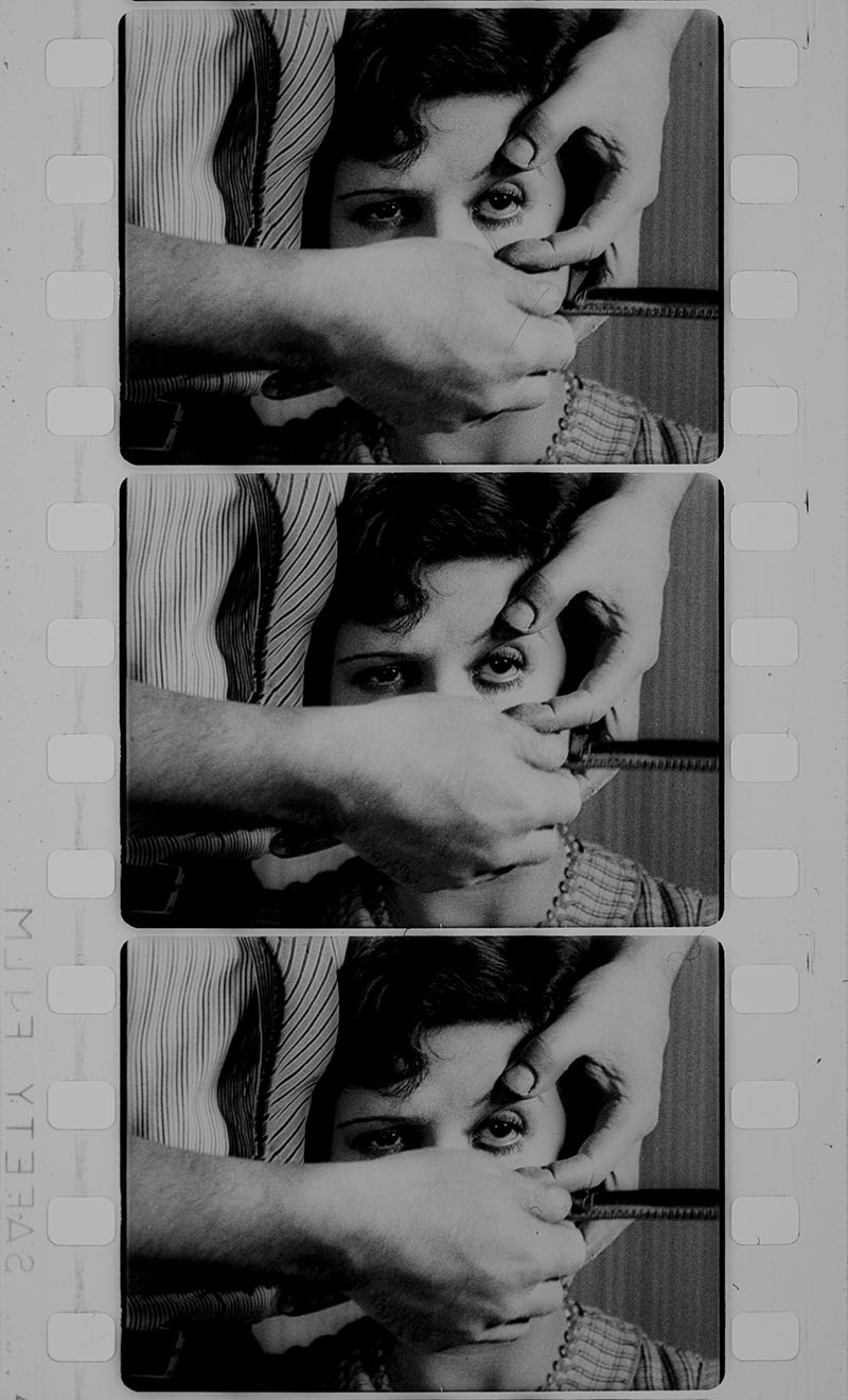 In this iconic sequence from the surrealist short film “Un Chien Andalou” (1929) by Luis Buñuel and Salvador Dalí, three black-and-white film stills are stacked vertically, capturing a disturbing and dreamlike moment. A woman stares blankly ahead while a man's hands hold her steady and prepare to bring an open razor blade close to her eye. His fingers spread her eyelids with surgical precision, while her expression remains eerily neutral. The neutral background enhances the claustrophobic and unsettling atmosphere. This scene, designed to shock, exemplifies surrealist cinema's fascination with violence, dreams, and symbolic transgression.
