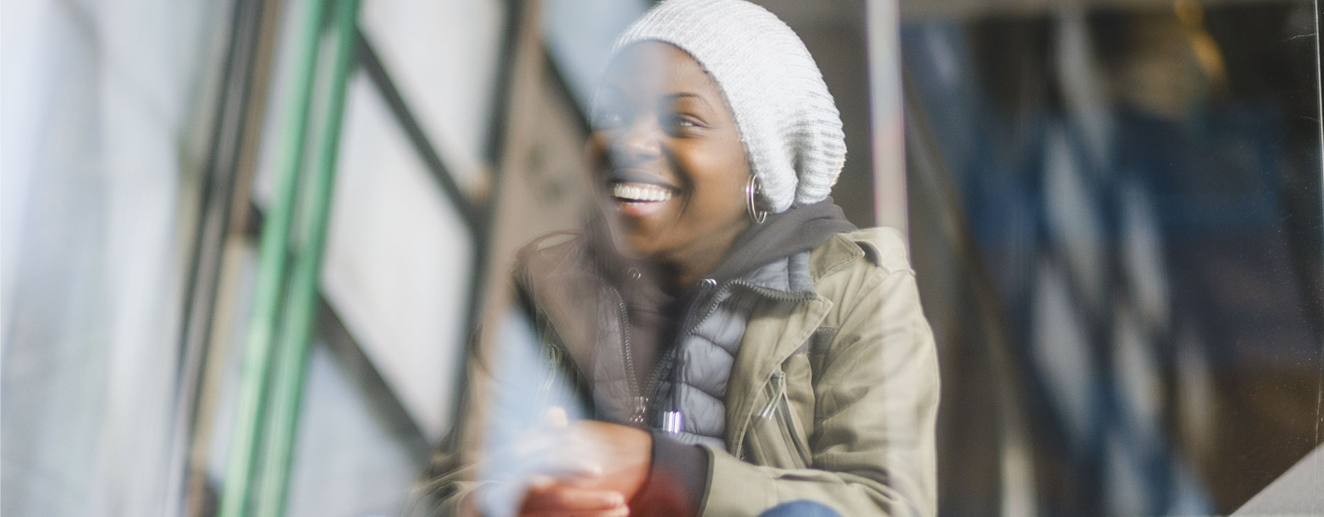 Josza Anjembe, réalisatrice franco-camerounaise, monte un escalator vitré du Centre Pompidou. En arrière-plan, les structures tubulaires emblématiques du bâtiment se dessinent sous une lumière douce. Son expression calme et assurée reflète la créativité et la détermination. L’ambiance urbaine et artistique du lieu amplifie la portée culturelle de la scène.