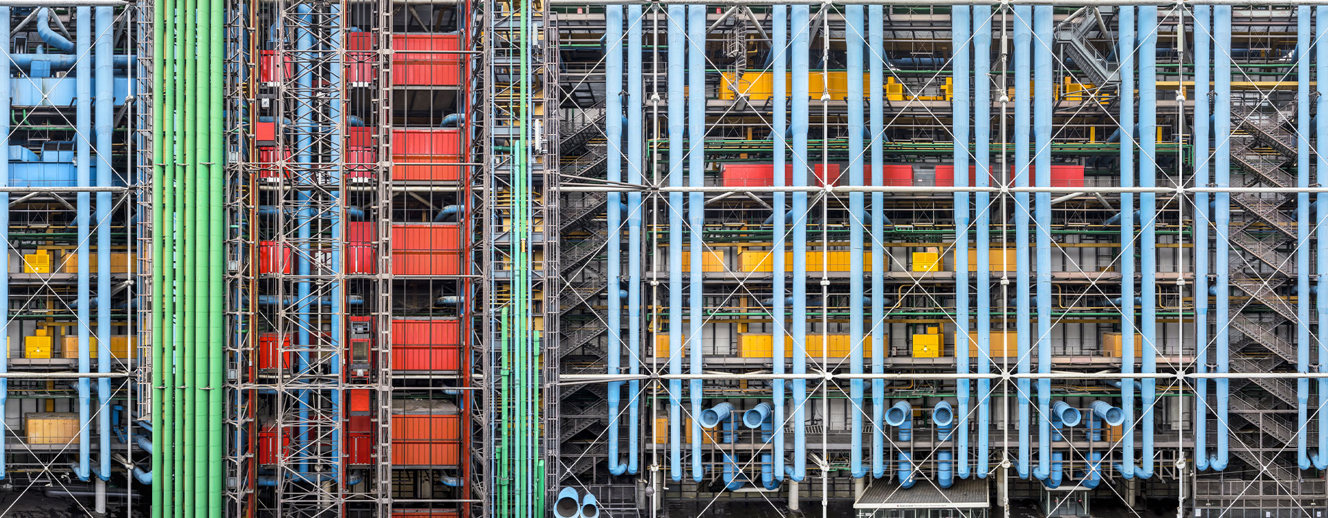 Façade avant du Centre Pompidou à Paris, avec son architecture industrielle haute en couleurs. Les tuyaux bleus, verts, rouges et jaunes ressortent sur la structure métallique apparente. Cette vision urbaine, dynamique et futuriste symbolise l'audace architecturale du bâtiment conçu par Renzo Piano et Richard Rogers.